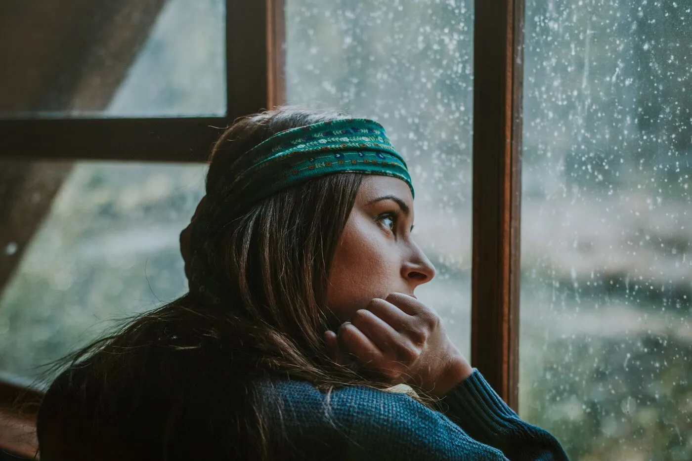 A woman gazes thoughtfully out a rain-flecked window
